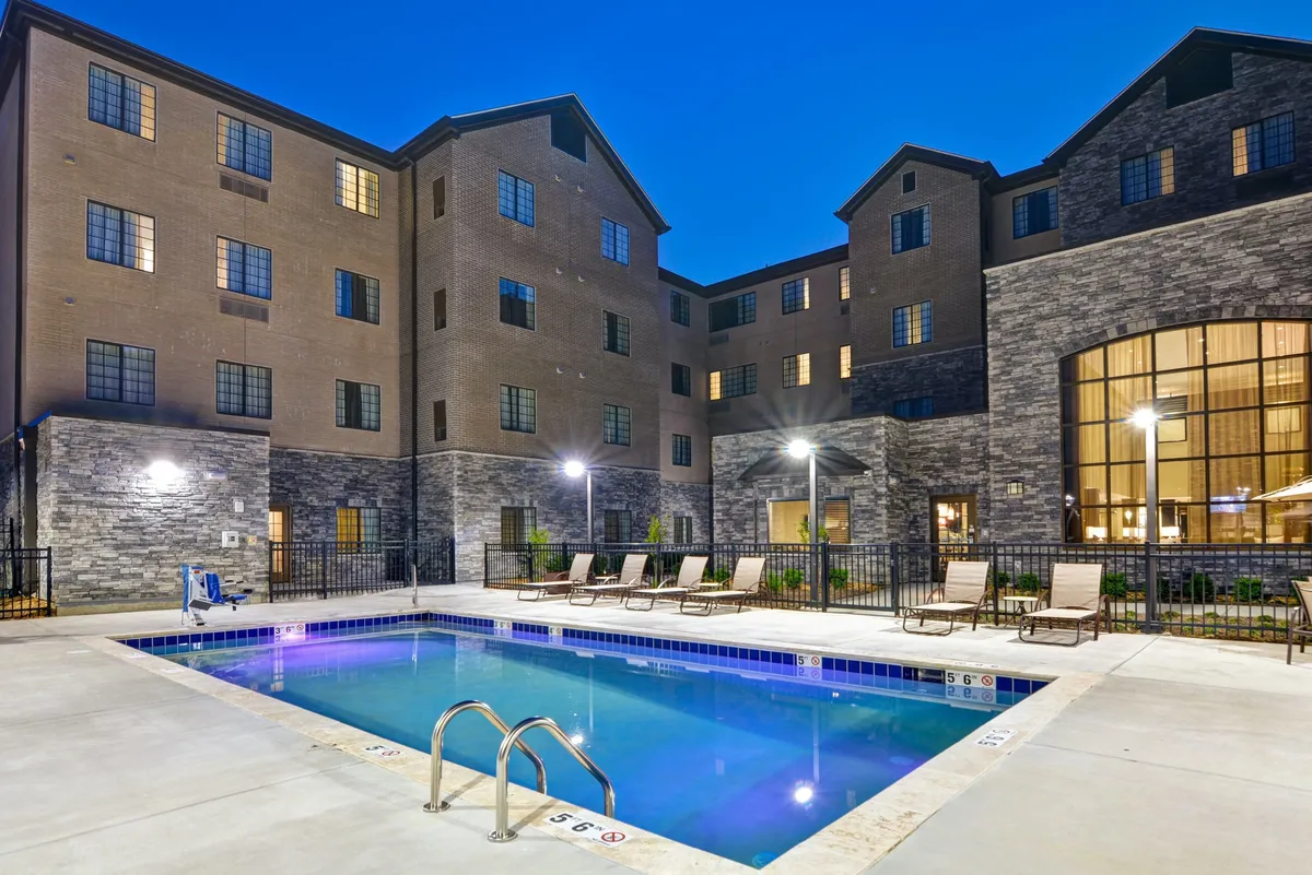 This image features the hotel's outdoor swimming pool surrounded by comfortable lounge chairs and the building's inviting facade. The relaxed atmosphere hints at sunset or early evening, with the pool ready for a refreshing dip or casual social gathering.