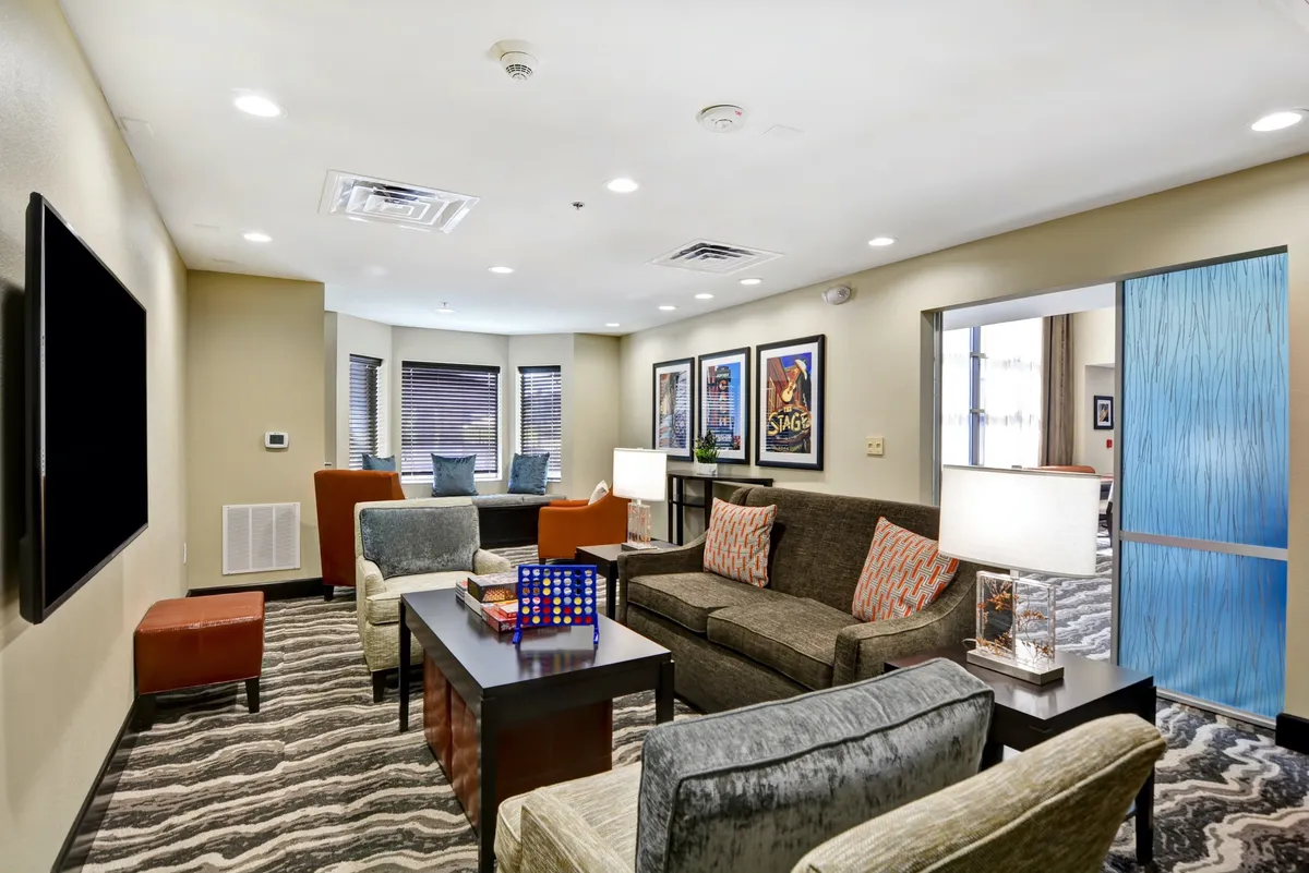 A warmly lit seating area furnished with a sofa, armchairs, a coffee table, and contemporary artwork on the walls. The setting feels welcoming and comfortable, ideal for quiet relaxation or casual conversation.