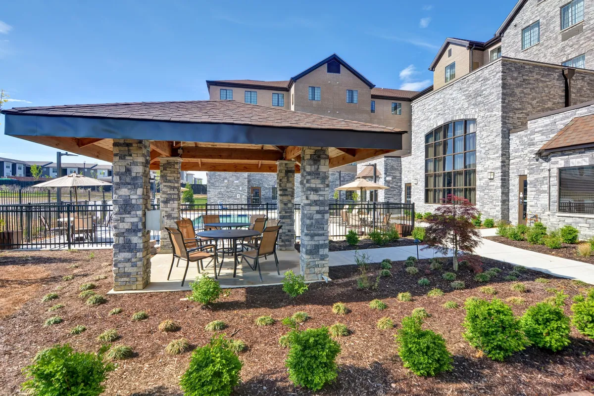 An exterior scene with a stone gazebo, outdoor dining table, greenery, and views of the pool area. The space invites social gatherings, alfresco dining, or tranquil moments in nature, perfectly bridging the transition from outdoor exploration to comfortable hotel living.