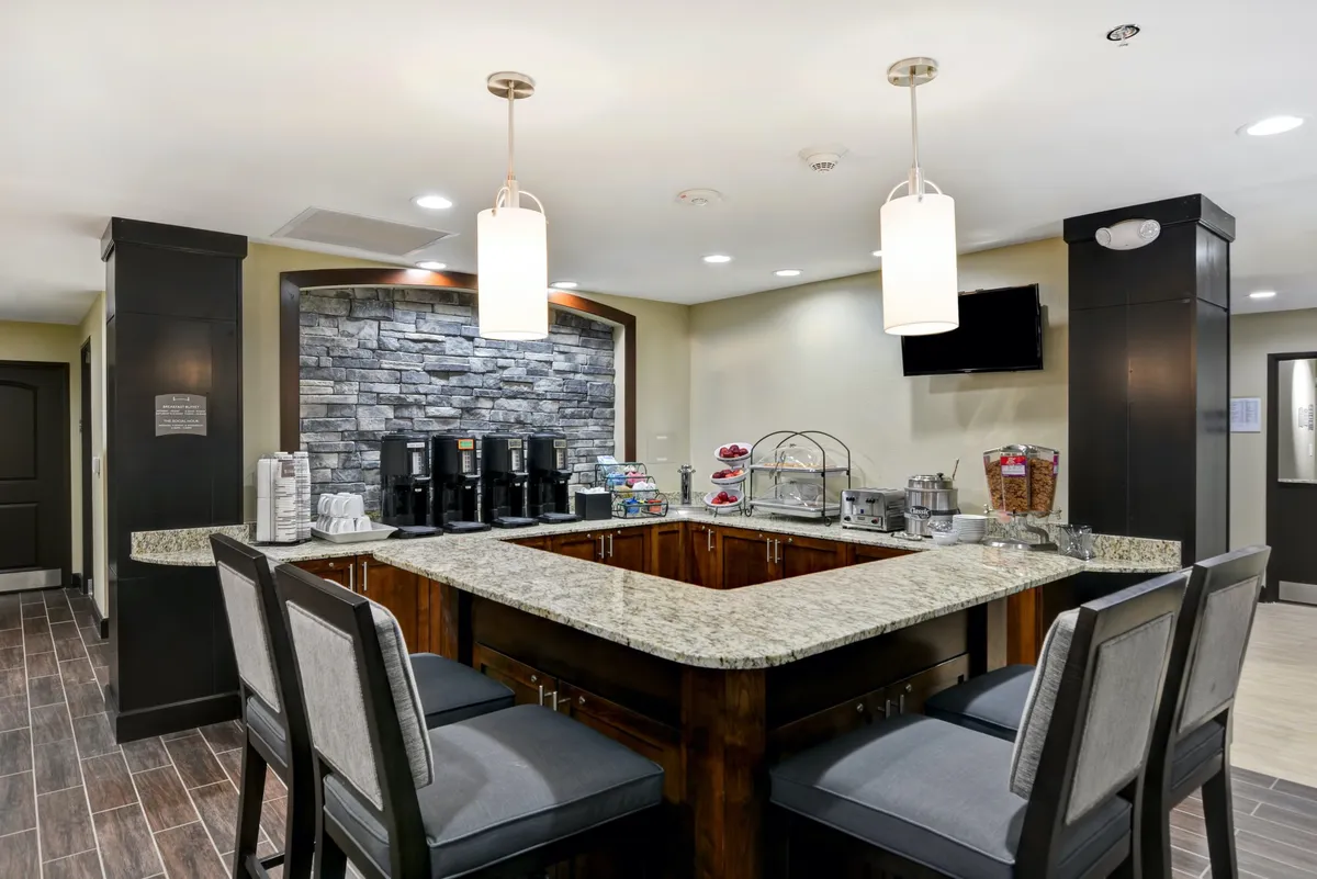 A granite countertop is the centerpiece of this image, with a coffee station, decorative stone wall, and stylish hanging light fixtures. The setup is clean and modern, evoking a welcoming kitchen atmosphere.