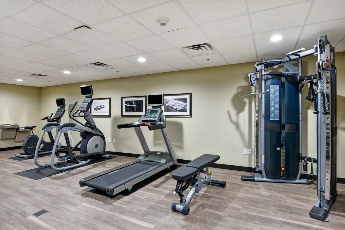 A modern, well-equipped fitness center featuring treadmills, an elliptical machine, weight bench, and a multi-gym station. The space is clean and organized, perfect for maintaining fitness routines anytime.