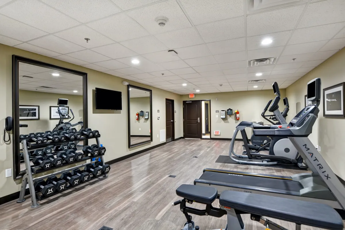 This image showcases a modern fitness center featuring a dumbbell rack, treadmills, elliptical machines, and mirrors. The setting appears spacious and accessible, supporting a range of fitness activities for guests of different abilities.