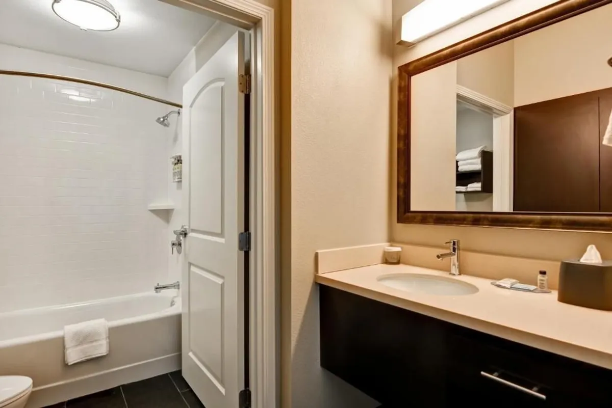 This image displays a contemporary bathroom interior with a well-lit sink and mirror, as well as a walk-in shower area. The clean lines, modern fixtures, and easy access highlight both style and functionality. Visible are plush white towels and a tidy countertop, contributing to the sense of comfort and convenience.