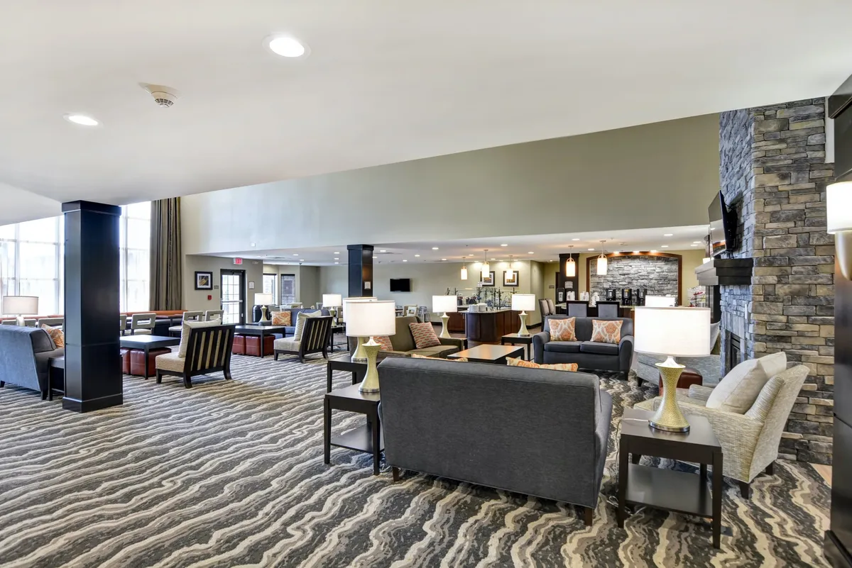 A cozy communal lounge featuring comfortable seating areas, modern lamps, a fireplace, and a textured accent wall. The atmosphere is inviting, perfect for socializing with family or relaxing after a day out.