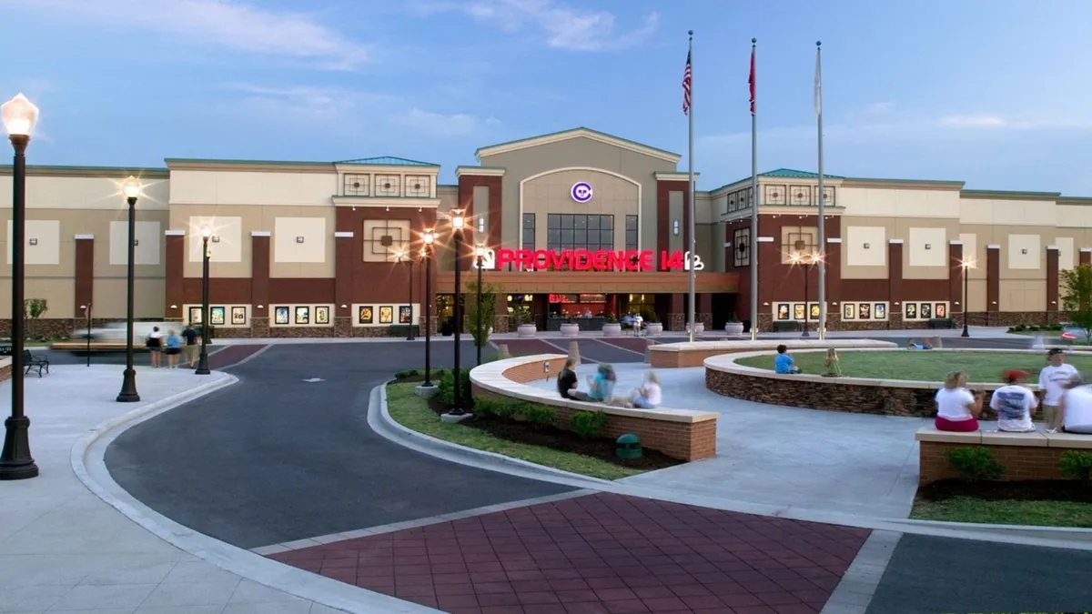 The main entrance of a cinema, featuring an illuminated sign and a landscaped plaza in front. The area is depicted in a lively, social setting, ideal for evenings out or catching a movie with colleagues or friends.